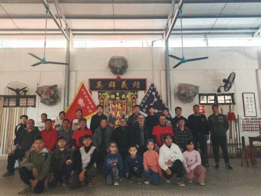 Die Cho-Familie in ihrer Trainingshalle: Erwachsene und Kinder unter der Tafel 結義群英 und den Fahnen des Cho-Kwoon